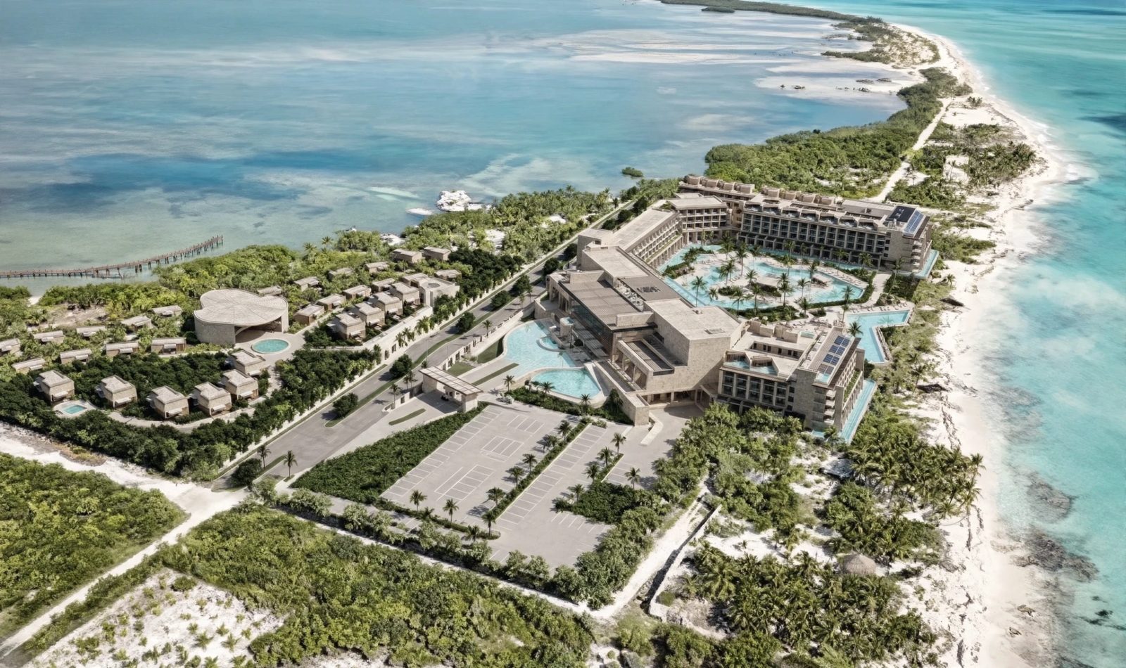 Aerial view of a beachfront resort complex on the Isla Blanca peninsula, with turquoise lagoon pools, palm groves, low-rise villas and a long dock reaching into the bay — Spa Life GC consulting project with Sunset World