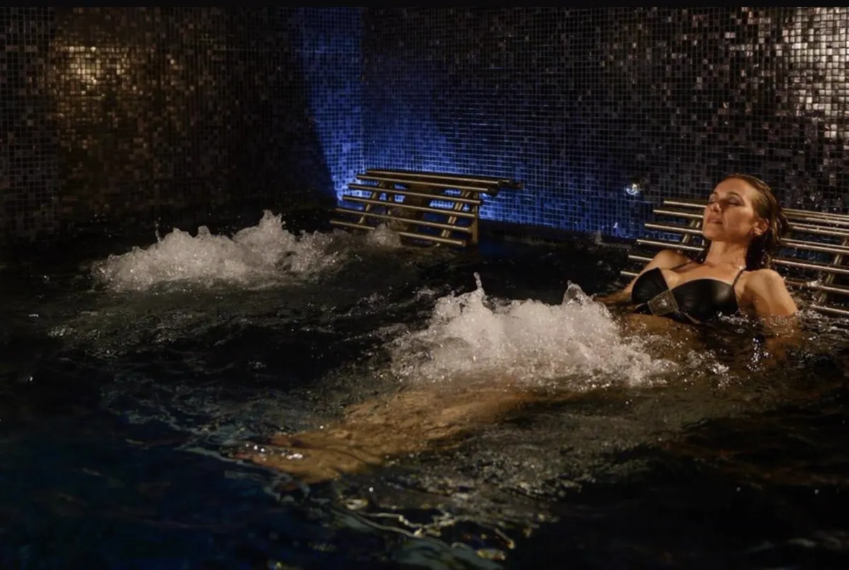 Guest relaxing on a hydrotherapy lounger in a dark tiled thermal pool with water jets — Spas de Grupo Brisas